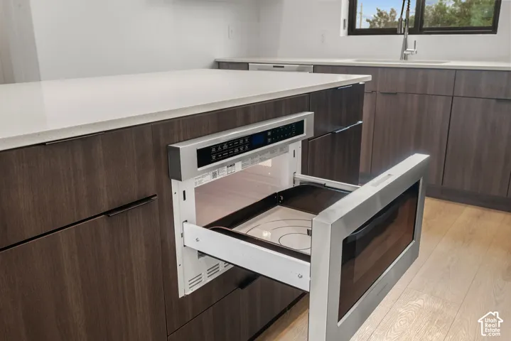 Kitchen featuring a built-in stainless steel microwave drawer, expansive stone-surface island, dark-toned cabinetry with integrated hardware, and wood-finish flooring