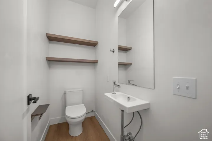 Wall-mounted washbasin with a polished chrome faucet, wood-finish flooring, floating wood-tone shelving, and a frameless wall mirror