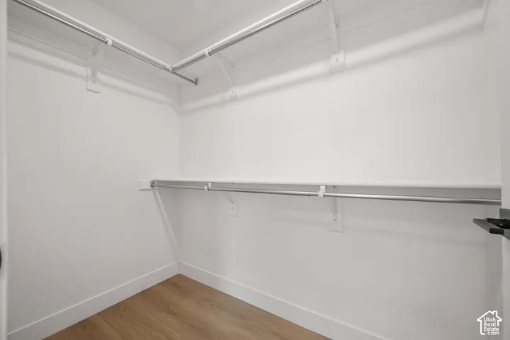 Walk-in closet featuring wood-finish flooring, dual-tier metal hanging rods, and integrated shelving