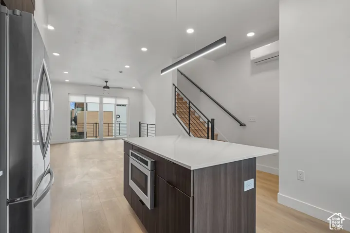 Kitchen featuring a central island with a solid surface countertop and built-in microwave, wood-finish flooring, recessed lighting, linear pendant lighting, and a staircase with a black metal railing