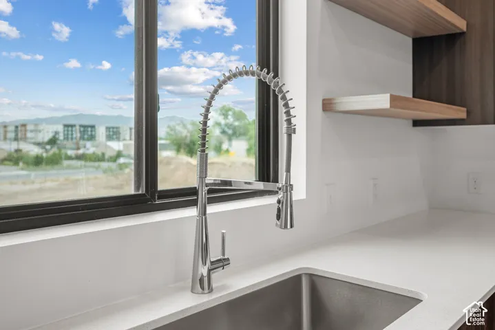 Stainless steel industrial-style pull-down faucet, undermount sink, solid surface countertop, and floating wood-finish shelving
