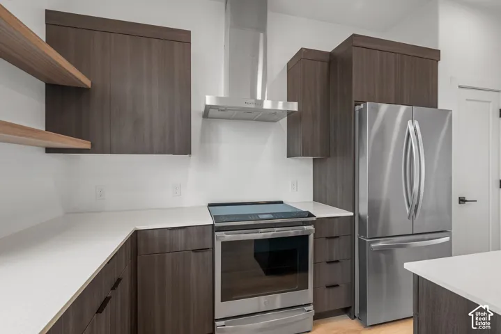 Kitchen featuring flat-panel cabinetry, open shelving, stainless steel appliances, a chimney-style range hood, and quartz countertops