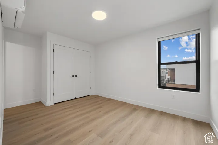 Interior space featuring light wood-finish flooring, double-door closet with matte black hardware, flush-mount circular lighting, and a window with black framing