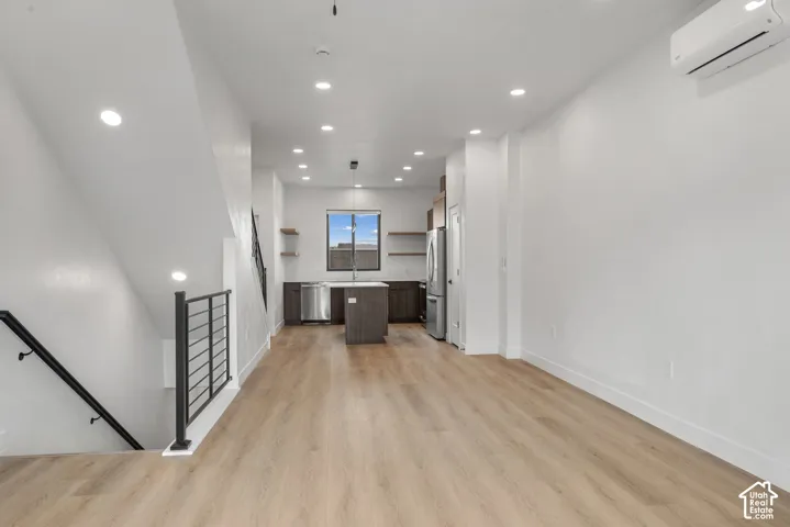 Open-concept area featuring wood-finish flooring, recessed lighting, a kitchen island with stone-surface countertop, custom cabinetry, and staircase with metal railing