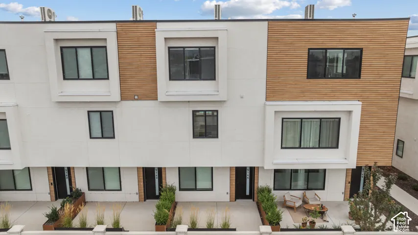 Contemporary multi-level exterior featuring white smooth-panel siding, horizontal wood-slat accents, recessed window bays, and private concrete patios with built-in metal planters
