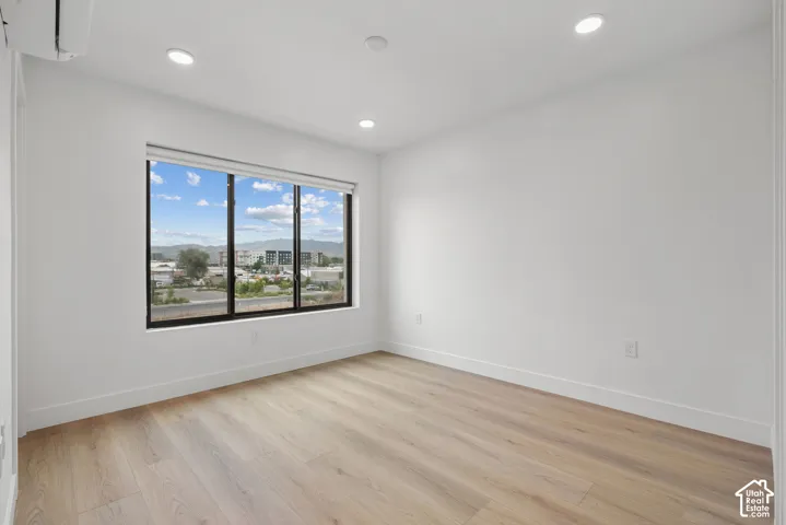 Interior space featuring wood-finish flooring, recessed lighting, a wall-mounted climate control unit, and a large window with exterior mountain scenery