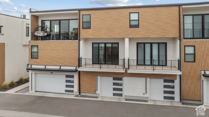 Contemporary multi-level exterior featuring horizontal wood-slat siding, smooth stucco finishes, tiered balconies with black metal railings, and multi-panel sectional garage doors
