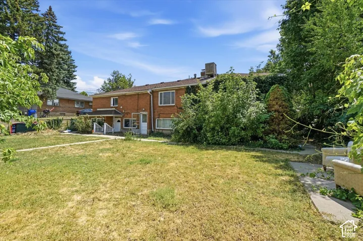 Brick exterior residence featuring a concrete patio, multiple entry points, and mature trees