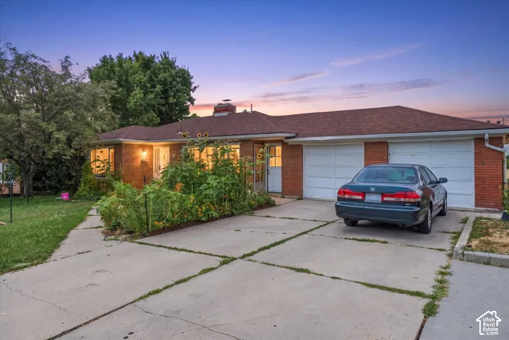 Rambler-style exterior featuring a brick facade, a shingled hip roof, a concrete driveway, and an attached two-car garage