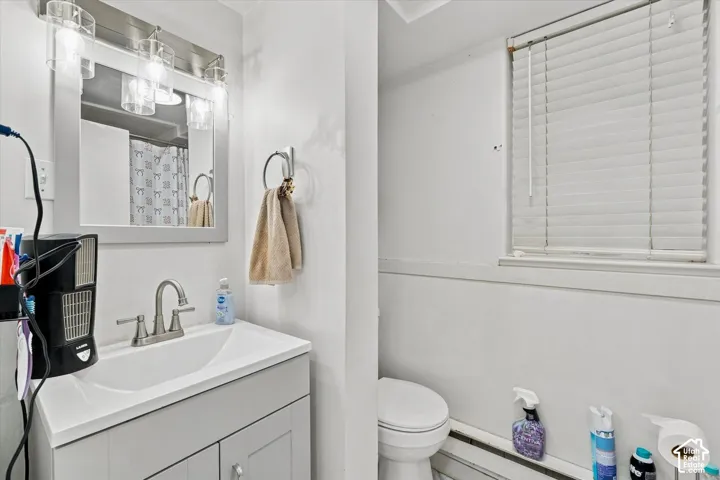 Bathroom featuring a shaker-style vanity, integrated rectangular sink, brushed nickel faucet, wall-mounted light fixture with glass shades, and horizontal blind window treatment
