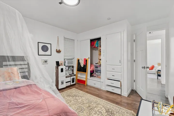 Bedroom featuring wood-finish flooring, recessed lighting, white built-in cabinetry with integrated drawers, and a sliding-door closet