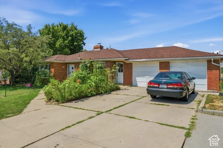 Single-story brick exterior featuring a multi-car garage, concrete driveway, and masonry chimney