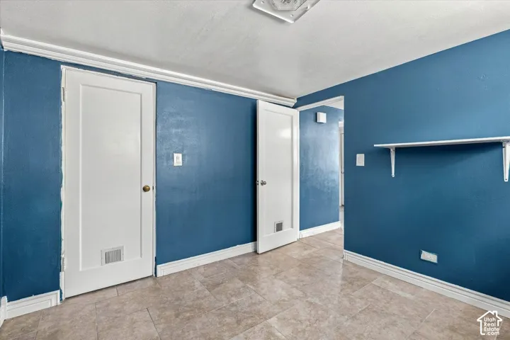 Interior space featuring stone-style tile flooring, two solid-core interior doors, crown molding, and a wall-mounted shelving unit