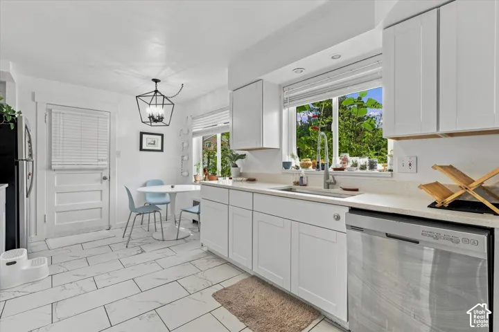 Kitchen featuring white shaker-style cabinetry, neutral stone-finish countertops, stainless steel undermount sink with gooseneck faucet, large-format tile flooring, and a geometric metal pendant light fixture