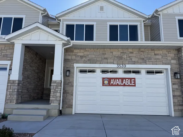 Exterior facade featuring horizontal siding and stacked stone masonry, gabled rooflines, a covered porch entrance with square columns, and a multi-panel garage door with transom windows