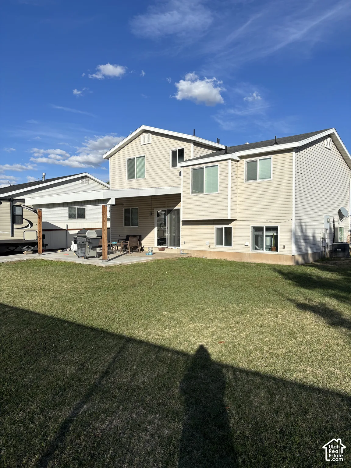 Rear exterior featuring light-toned horizontal siding, a covered concrete patio, and a grass lawn