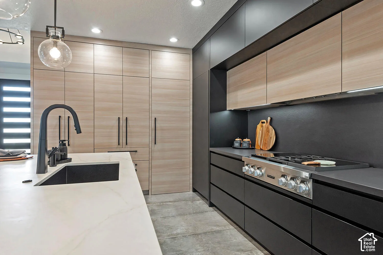 Kitchen featuring matte black flat-panel cabinetry, light wood-finish floor-to-ceiling storage, a central island with a quartz countertop, a deep undermount sink, and a high-performance gas range