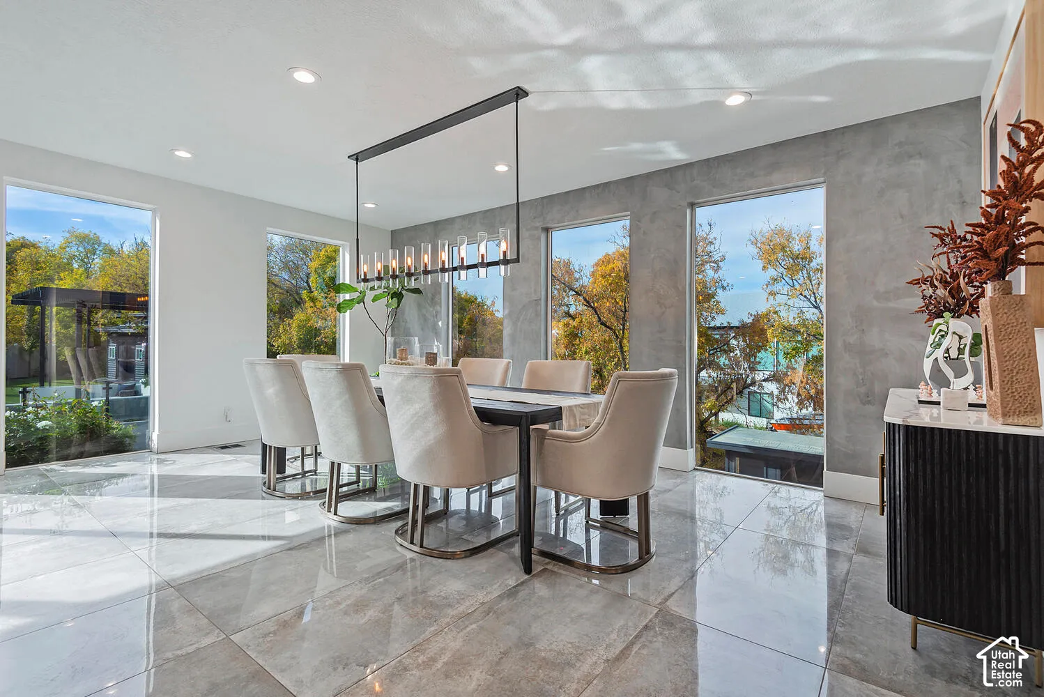 Dining area featuring polished large-format tile flooring, a textured gray accent wall, floor-to-ceiling windows, and a multi-pendant linear light fixture