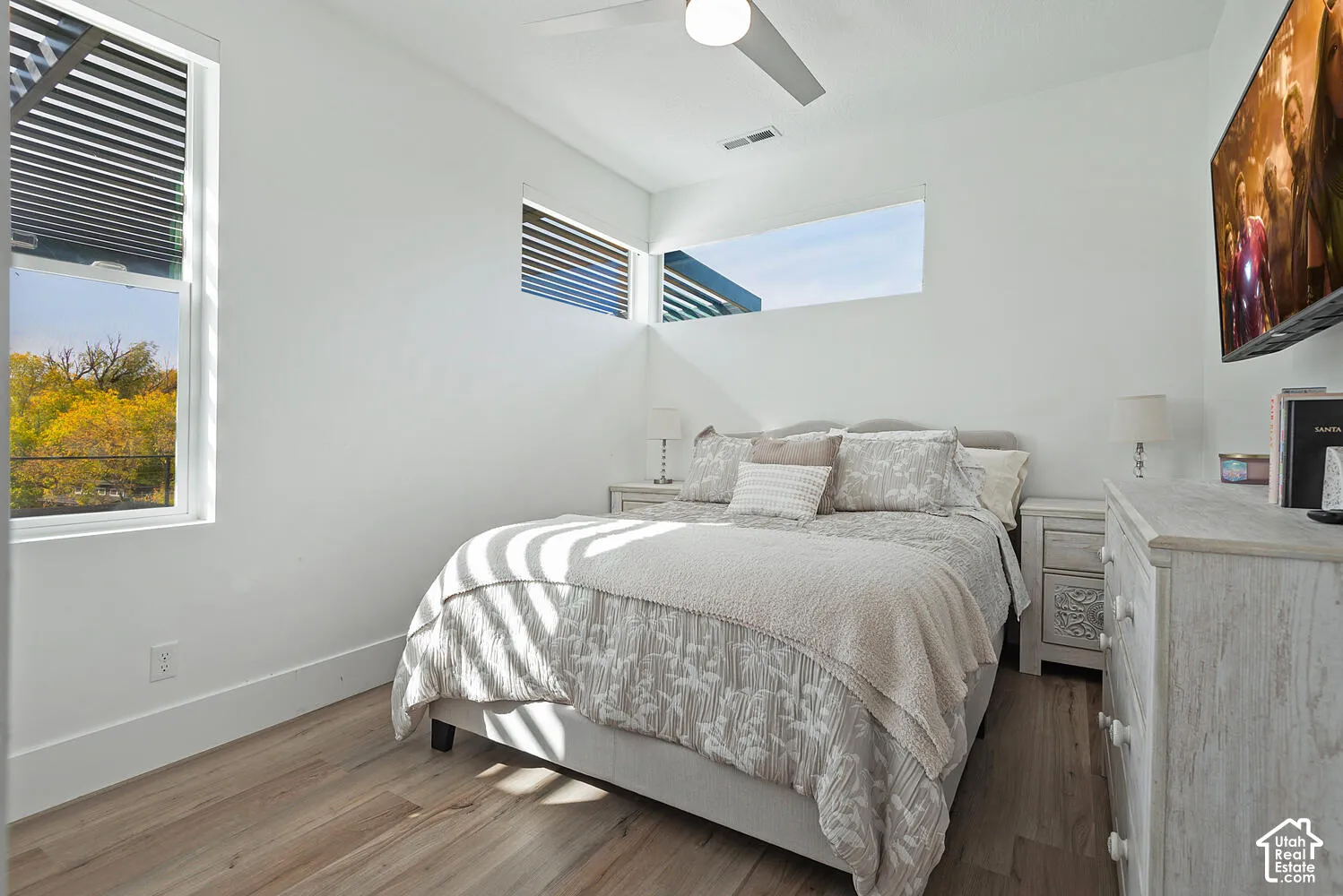 Wood-finish flooring, corner ribbon windows, tall vertical window, and ceiling fan with integrated lighting