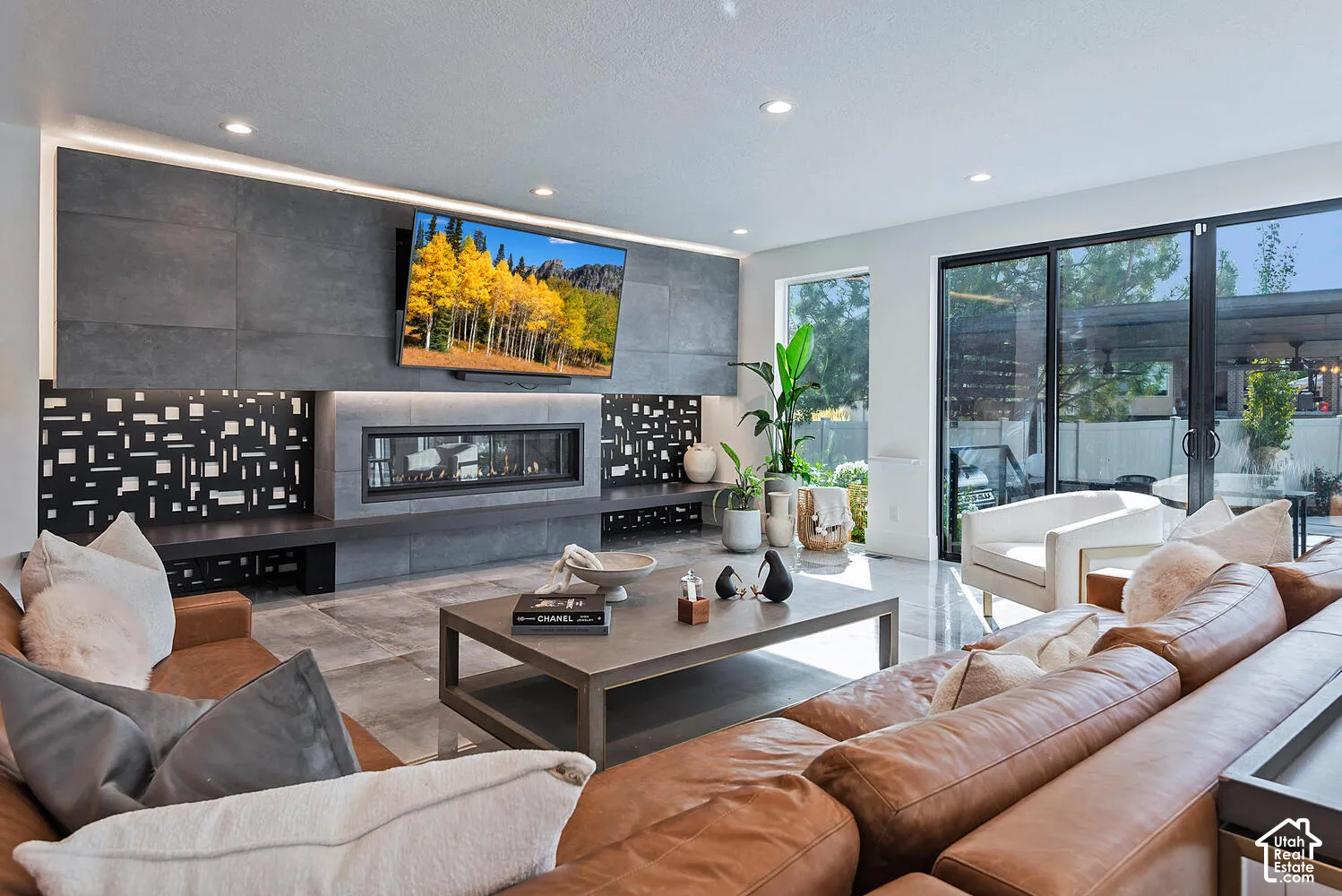 Large format stone tile flooring, floor-to-ceiling multi-panel glass sliding doors, built-in linear fireplace with stone cladding, decorative metal paneling, and recessed ceiling lighting