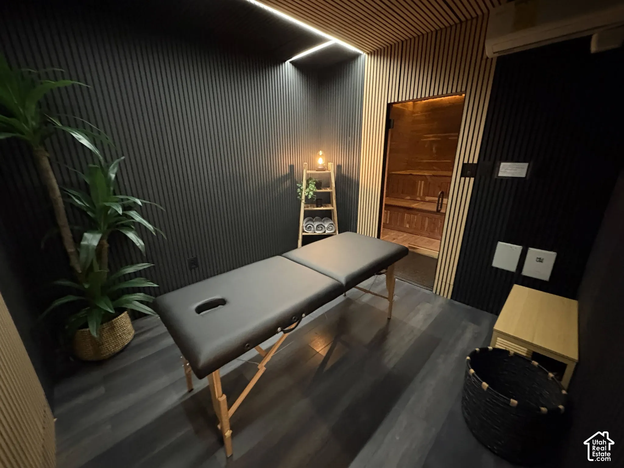 Custom interior featuring black and light wood-tone slatted wall paneling, linear recessed ceiling lighting, dark wood-finish flooring, and a built-in sauna with glass door entry