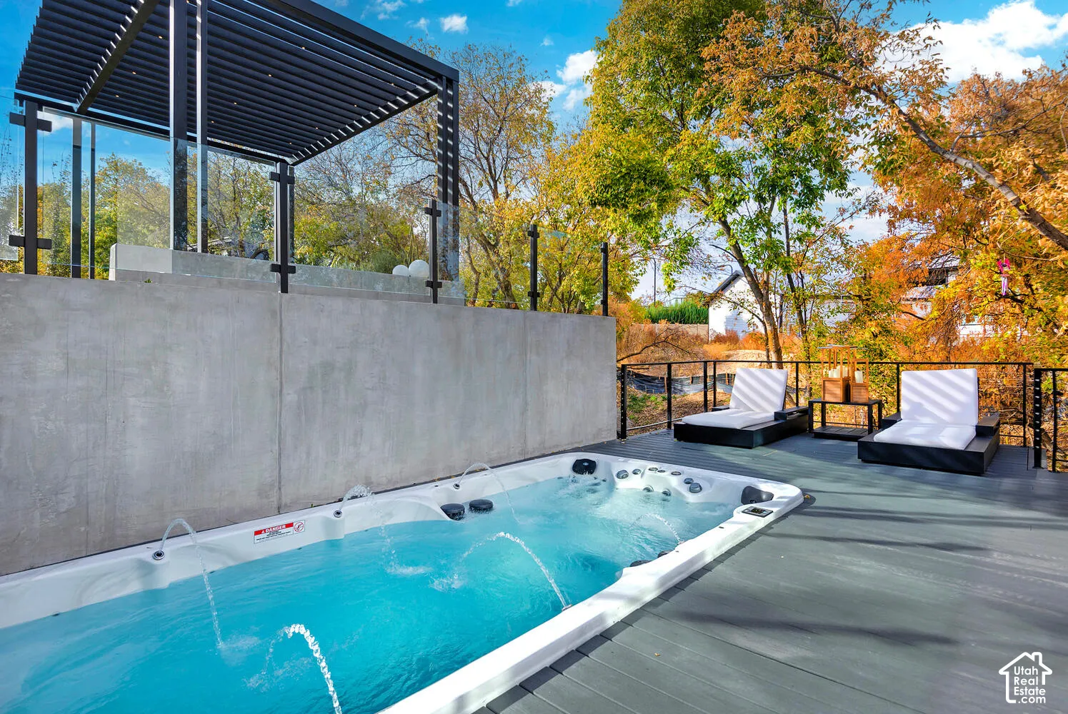 Elevated deck featuring a built-in swim spa, concrete retaining wall, metal pergola, and cable railing system