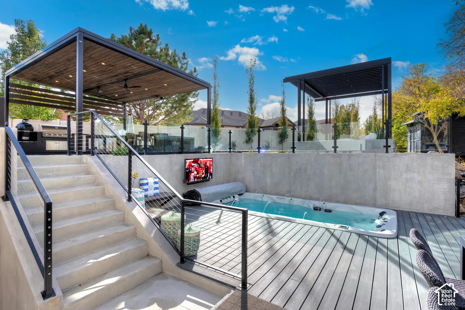 Multi-level outdoor living space featuring a built-in spa, elevated covered pavilion, integrated kitchen area, and cable railing system