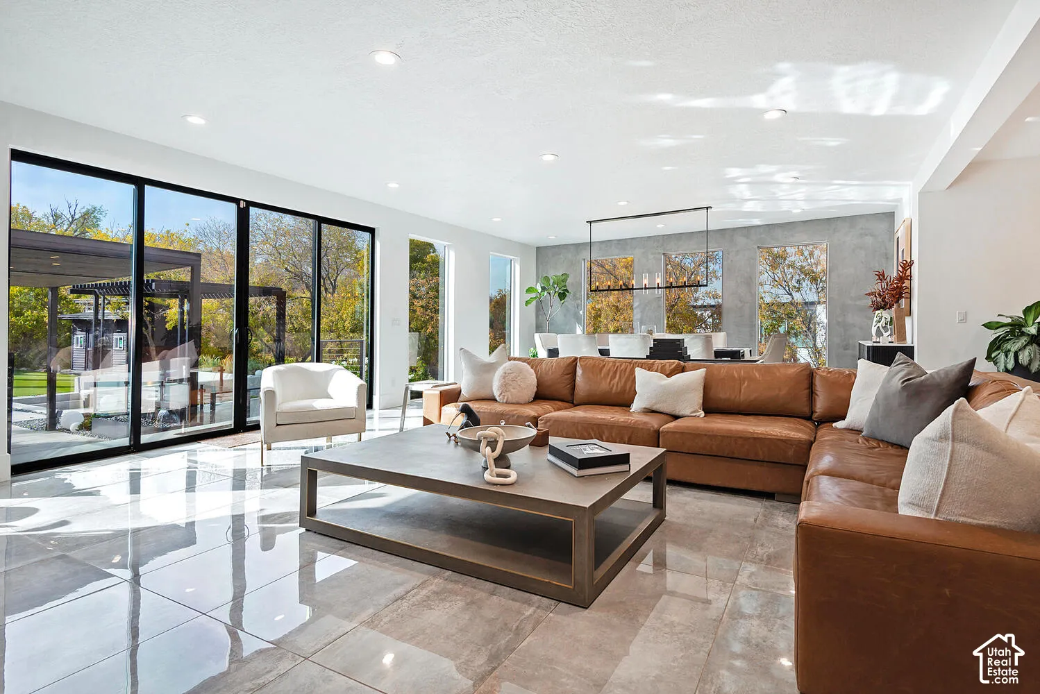 Open-concept living space featuring large-format tile flooring, expansive sliding glass walls, recessed lighting, and a textured accent wall