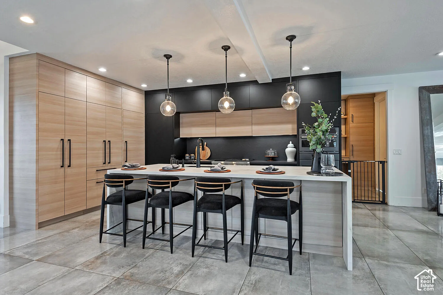 Kitchen featuring dual-tone cabinetry with wood-finish and matte black finishes, a large central island with a waterfall-edge countertop, matte black hardware, and three globe-style pendant lights