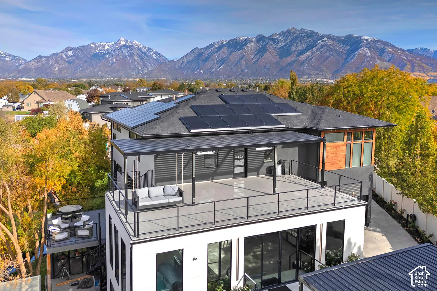 Elevated rooftop deck featuring metal railings, overhead pergola, and integrated solar panels, set against a prominent mountain backdrop