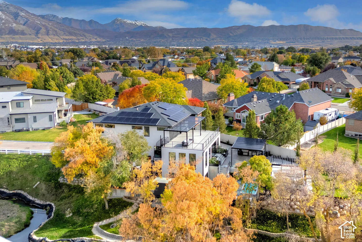 Multi-level residential exterior featuring rooftop solar panels, second-story balcony with metal railings, hardscaped patio, and mountainous backdrop