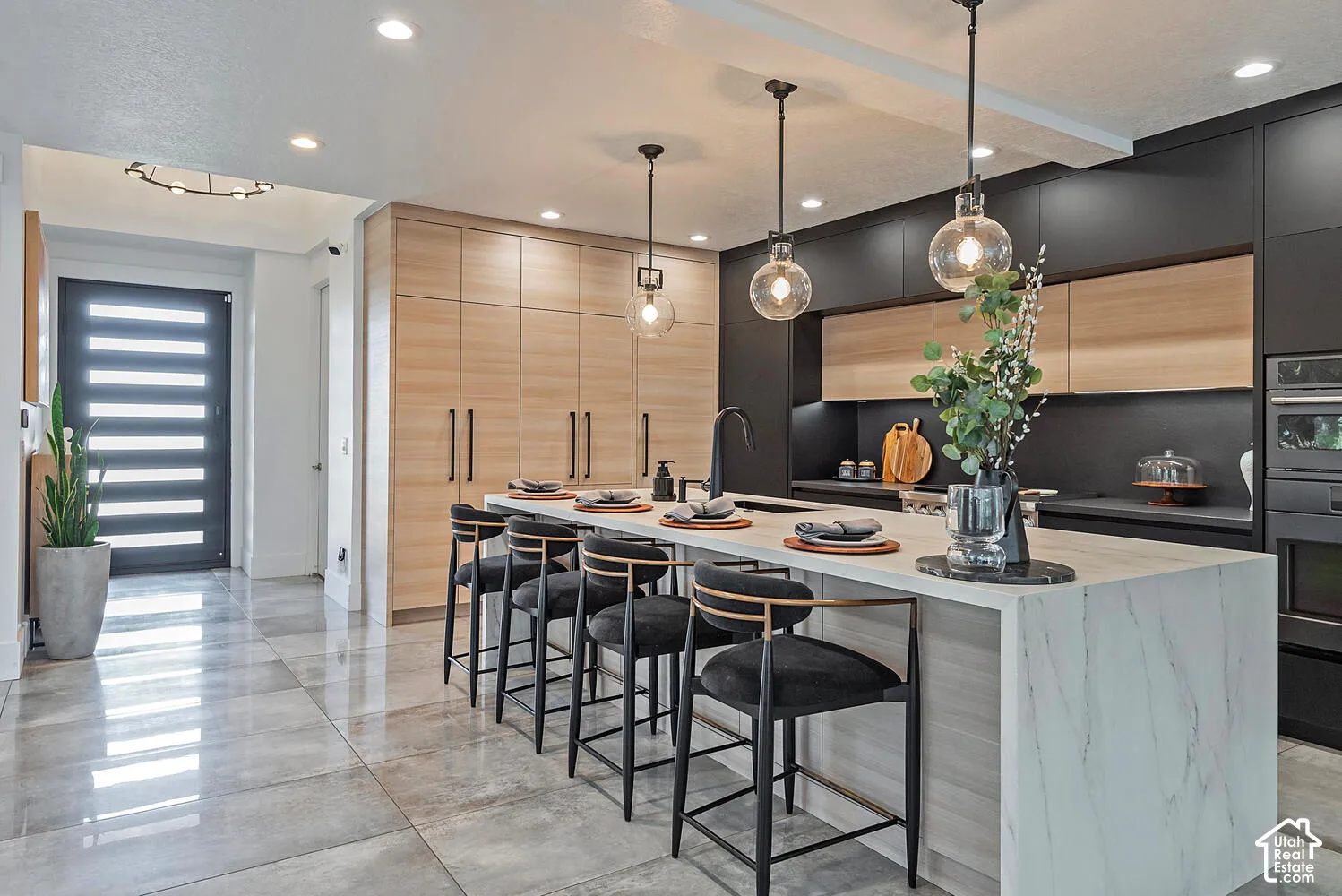 Kitchen featuring a waterfall-edge island with stone-finish countertop, two-tone custom cabinetry, recessed lighting, glass pendant fixtures, and large-format tile flooring