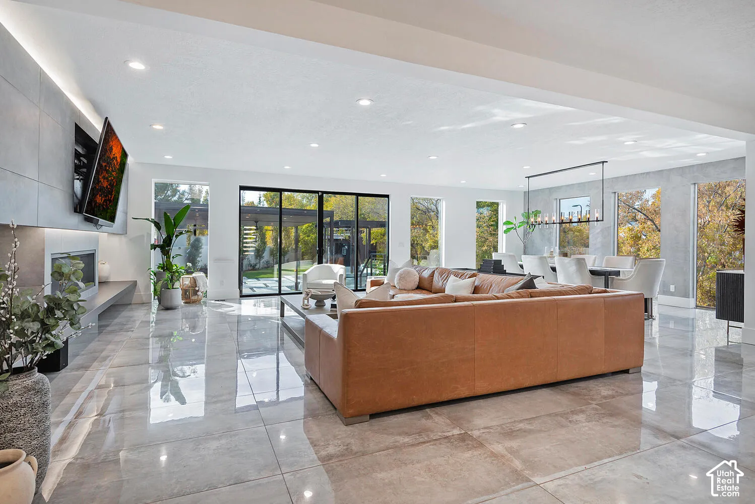 Open-concept floor plan featuring large-format polished tile flooring, a floor-to-ceiling accent wall with integrated linear fireplace, recessed lighting, and multi-panel sliding glass doors
