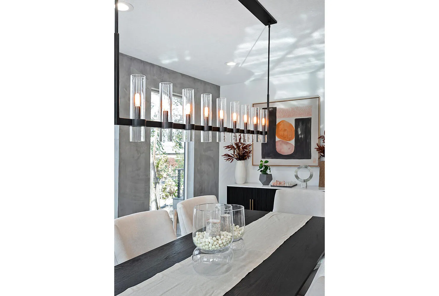 Linear multi-light pendant fixture featuring cylindrical glass shades and a matte black finish, accented by an architectural textured gray wall finish