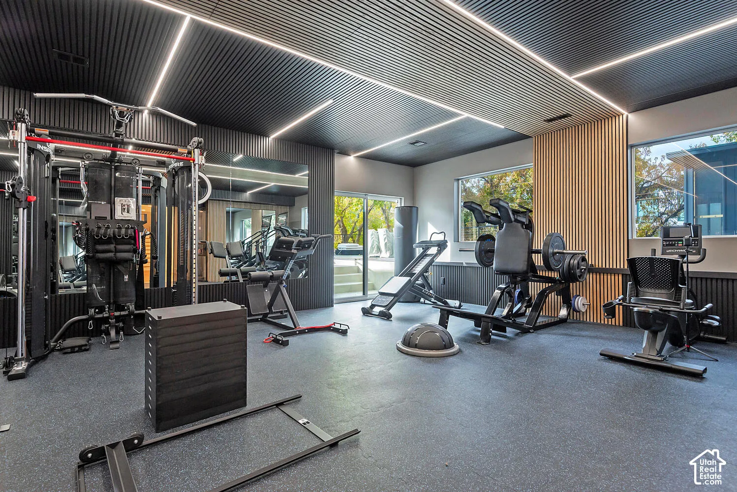 Black corrugated ceiling panels with integrated linear LED lighting, slatted wood wall detailing, large-format mirrored wall, and durable rubberized flooring
