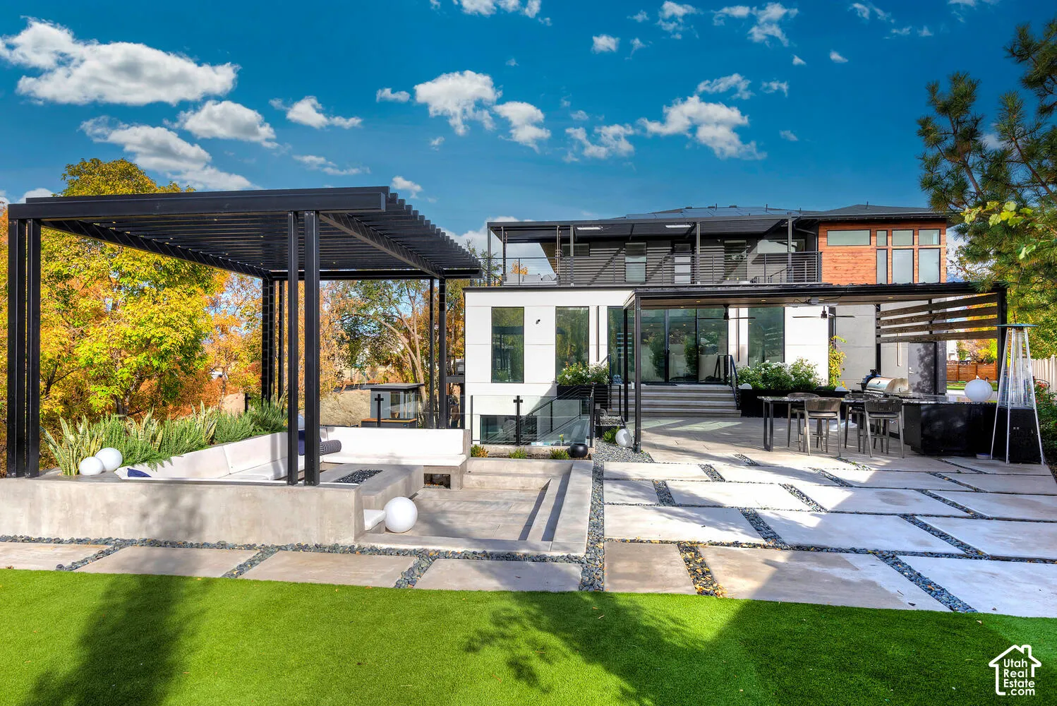 Hardscaped outdoor living area featuring a sunken concrete lounge, pergola, integrated built-in kitchen, and expansive paver patio
