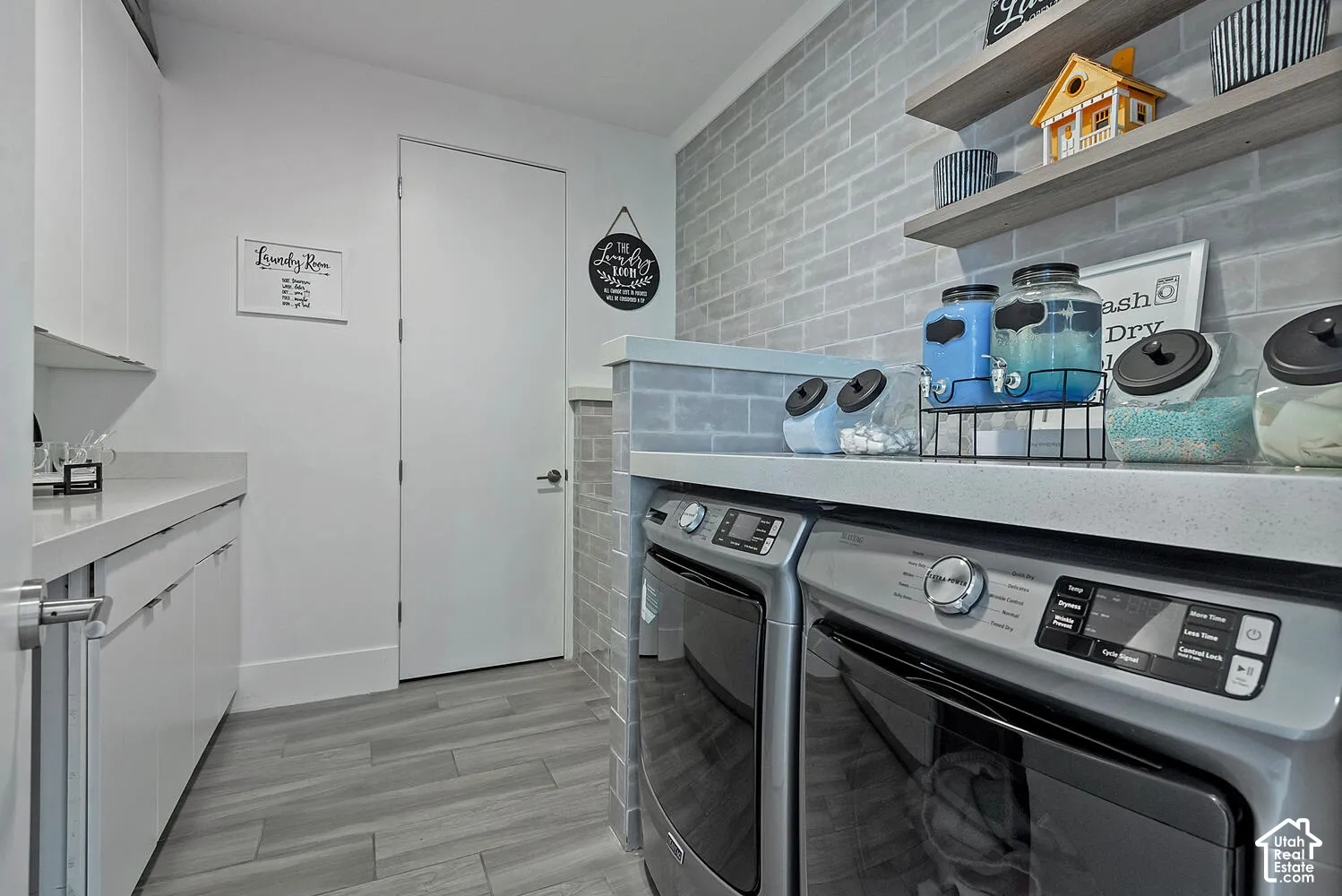 Laundry area featuring light-toned cabinetry, quartz countertops, gray subway tile backsplash, wood-finish flooring, and wall-mounted floating shelves