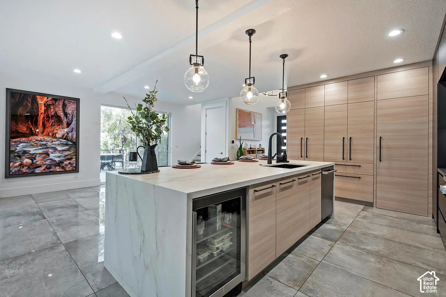 Kitchen featuring floor-to-ceiling cabinetry, a central island with a waterfall countertop, integrated beverage refrigerator, large-format tile flooring, and glass globe pendant lighting