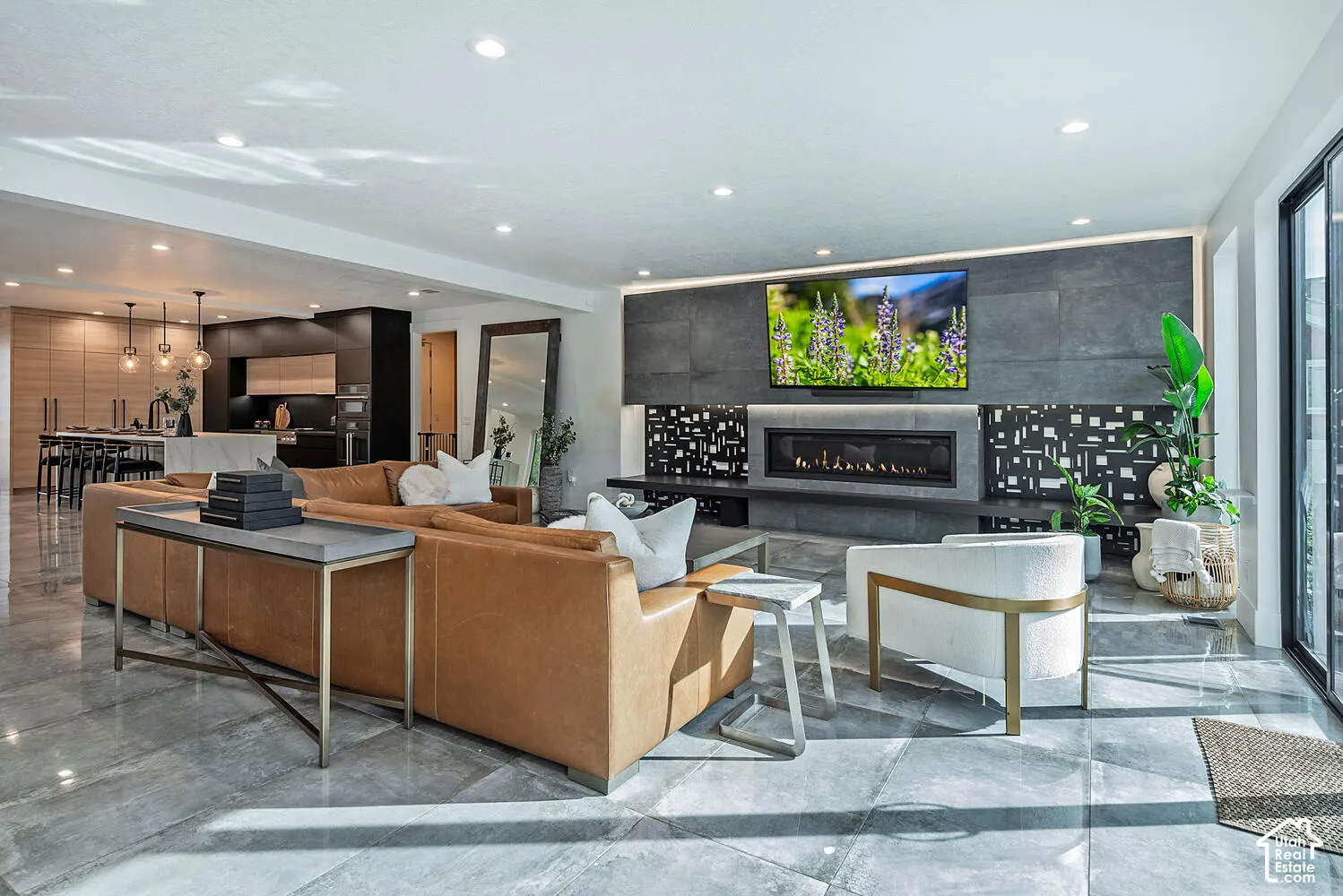 Open-concept interior featuring large-format tile flooring, a floor-to-ceiling stone fireplace surround with a linear hearth, recessed lighting, and built-in minimalist cabinetry
