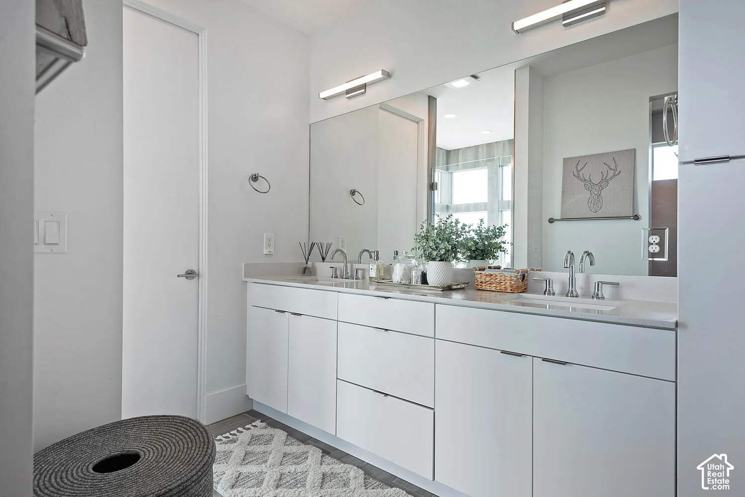 Dual-sink vanity featuring flat-panel cabinetry, light-toned stone countertops, polished chrome widespread faucets, and full-width vanity mirror with integrated LED bar lighting