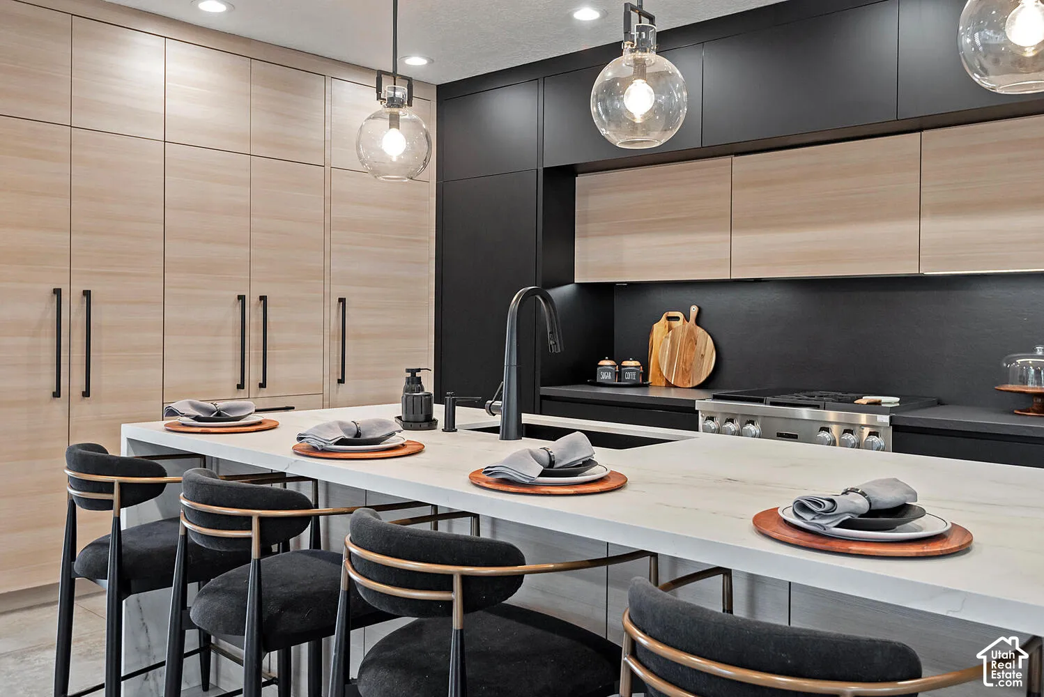 Kitchen featuring floor-to-ceiling wood-finish cabinetry, matte black flat-panel cabinetry, a central island with a solid surface countertop, integrated professional-grade gas range, and spherical pendant lighting