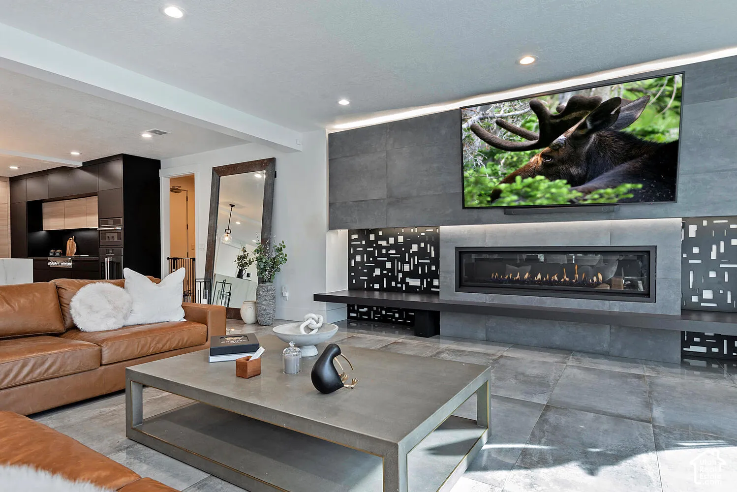 Living area featuring large-format tile flooring, a floor-to-ceiling stone-clad fireplace wall with integrated linear firebox, decorative patterned metal paneling, and recessed ceiling lighting