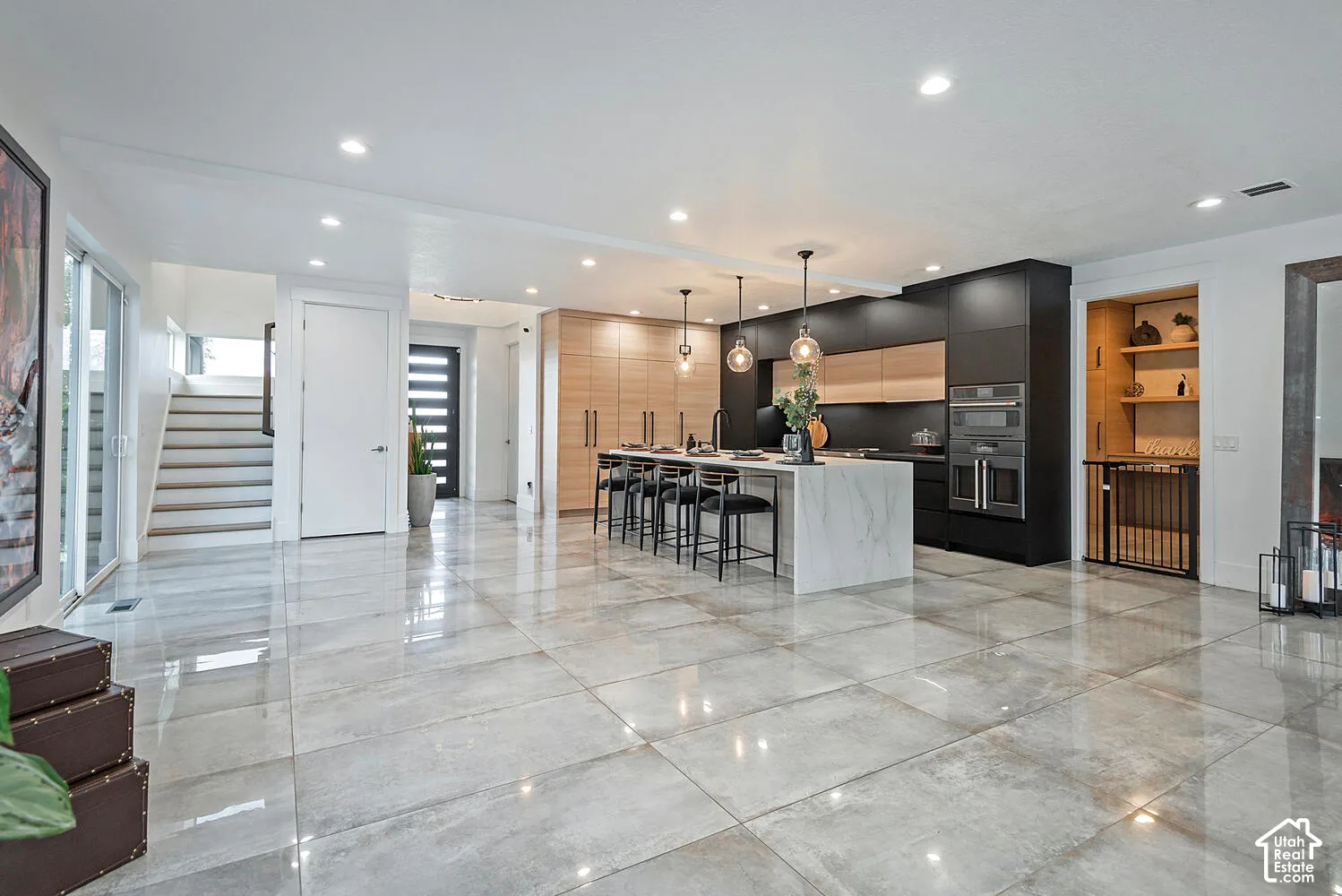 Modern kitchen featuring large-format tile flooring, dual-tone cabinetry, a waterfall-edge center island, built-in stainless steel double ovens, and recessed lighting
