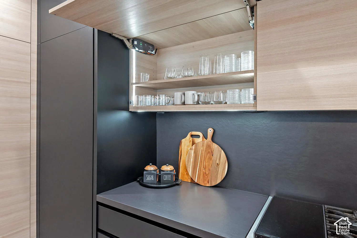Custom cabinetry featuring horizontal wood-finish grain, matte charcoal surfaces, upward-opening pneumatic cabinet doors, and integrated under-cabinet lighting