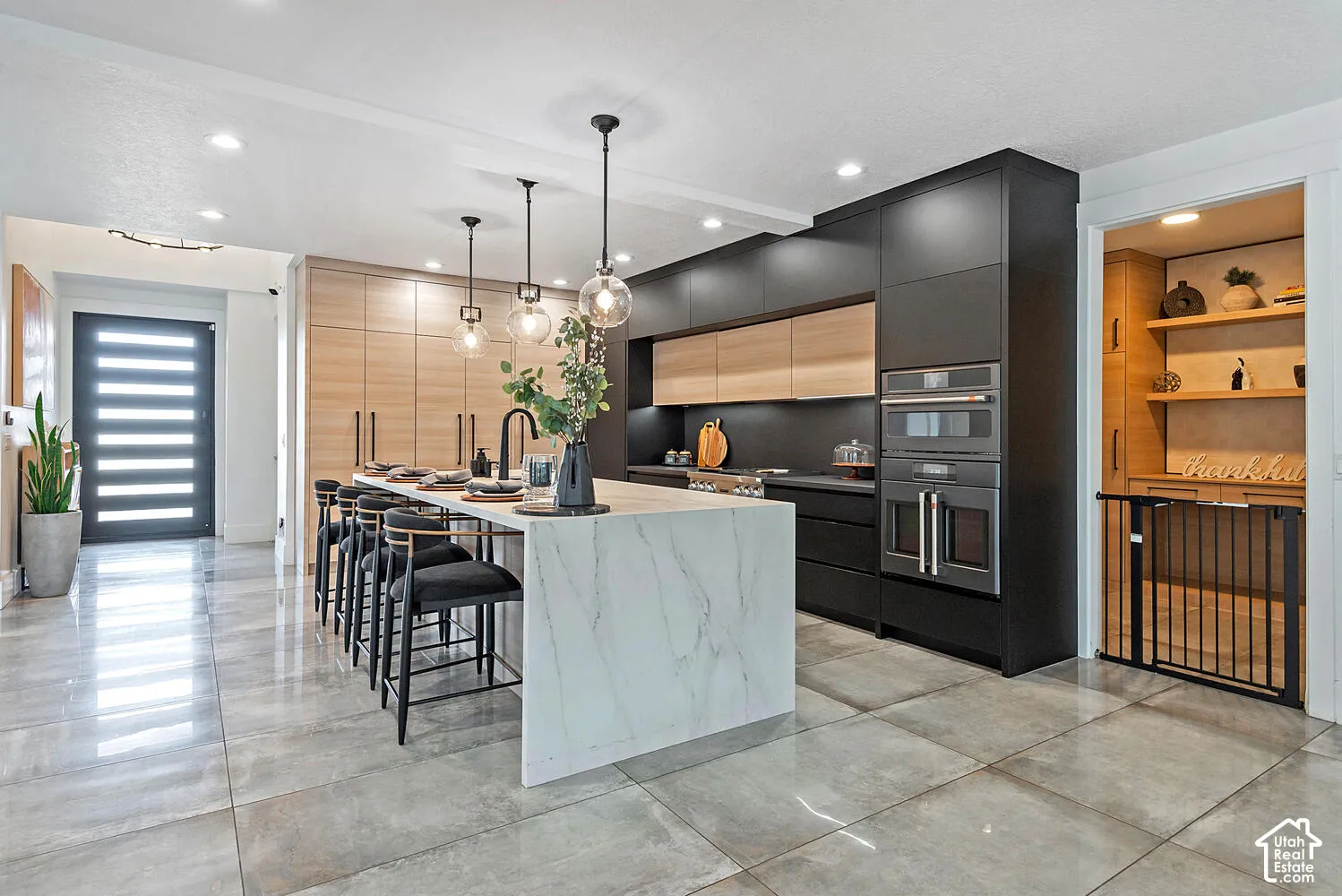 Kitchen featuring a waterfall-edge island with stone-finish countertop, matte black cabinetry, light-toned built-in storage, recessed lighting, and large-format tile flooring