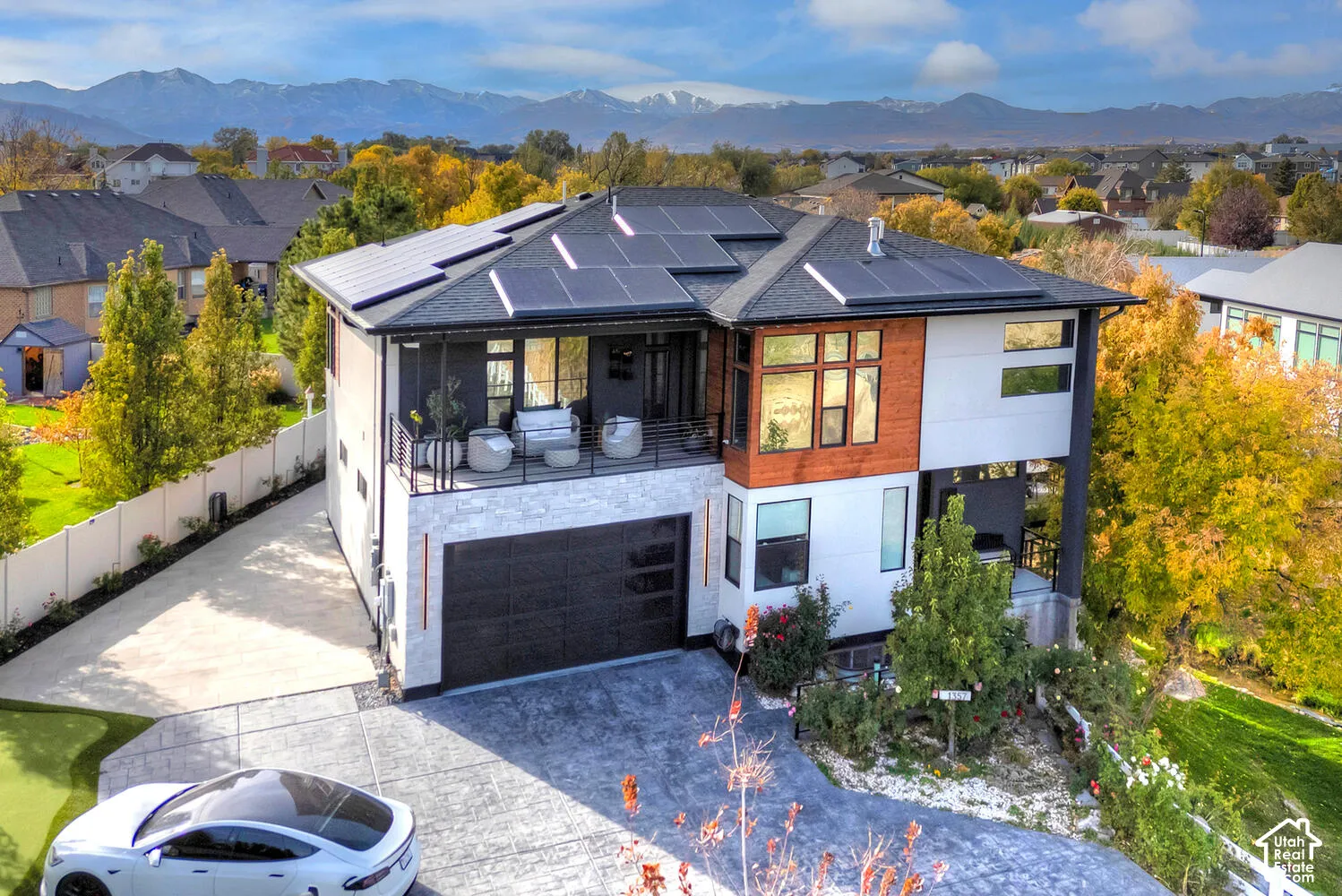 Multi-level contemporary exterior featuring stone veneer accents, wood-tone siding, a rooftop solar array, a covered balcony with metal railing, and a stamped concrete driveway