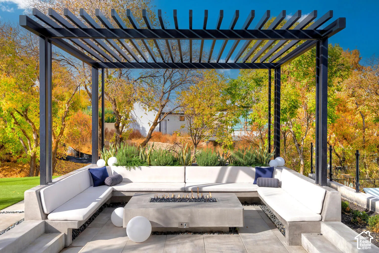 Outdoor pergola structure featuring a concrete fire pit, tiered concrete bench seating, stone-paver flooring, and manicured landscaping