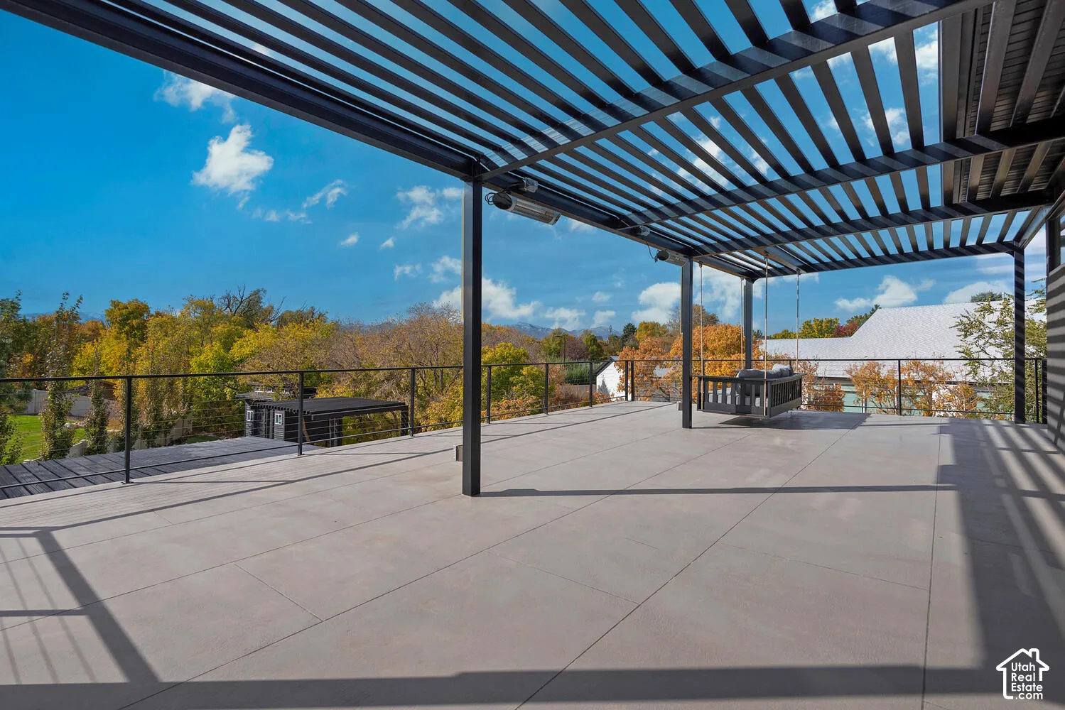 Expansive deck featuring large-format tile flooring, a black metal louvered pergola, and thin-profile black metal railings