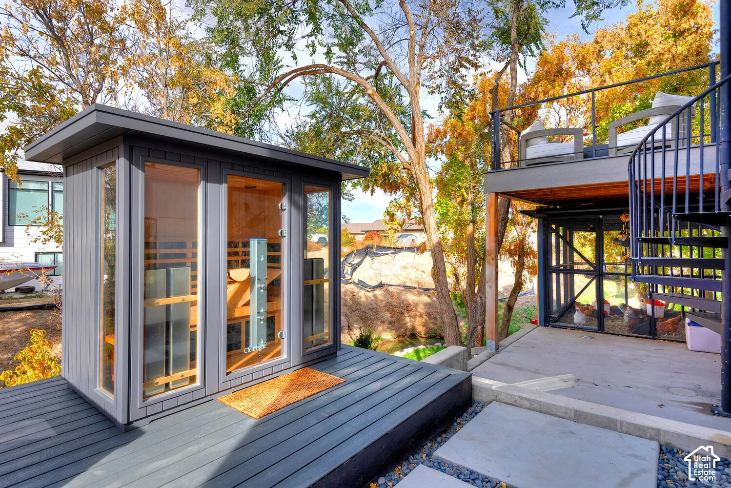 Outdoor sauna featuring a glass-front design, dark composite decking, an elevated balcony with metal railings, a spiral staircase, and a dedicated enclosure area