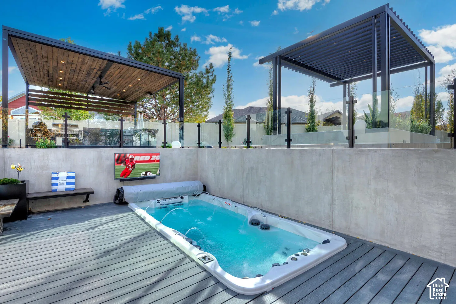 Custom-built outdoor space featuring a recessed aquatic fitness unit, composite decking, dual metal-framed pergolas, and a concrete retaining wall with glass safety panels